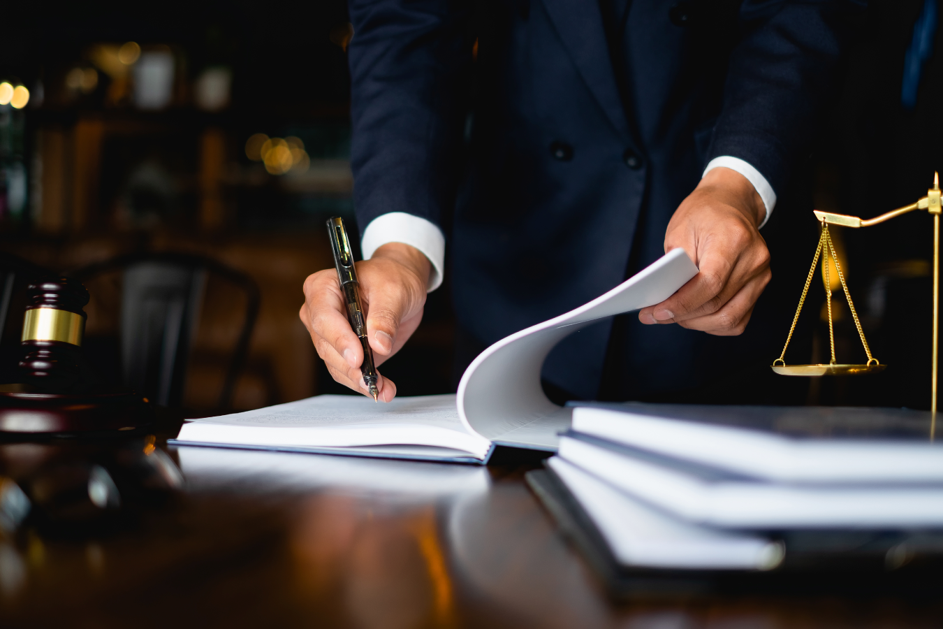 Person writing in a notebook on a desk with a gavel and justice scales