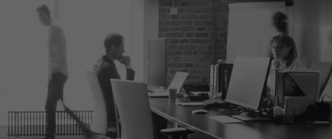Employees working in open office with desks and computers, blurred coworkers in background for modern workplace collaboration