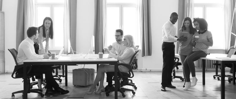 Coworkers collaborating in open office workspace with desks and laptops, team discussion and modern workplace productivity