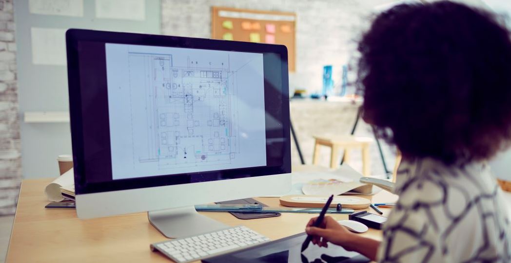 Designer reviewing architectural floor plan on desktop computer, working on office layout and building design project at workstation