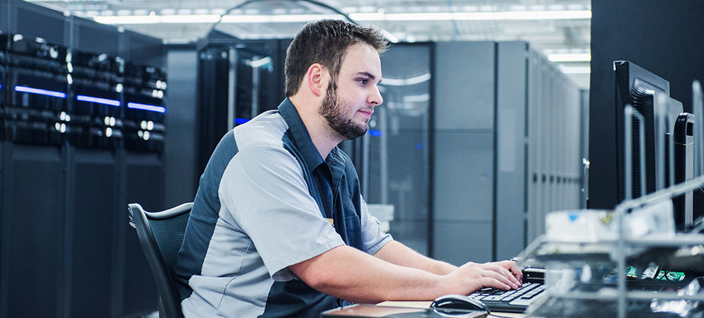 IT technician working at computer in data center server room, monitoring network systems and managing enterprise infrastructure