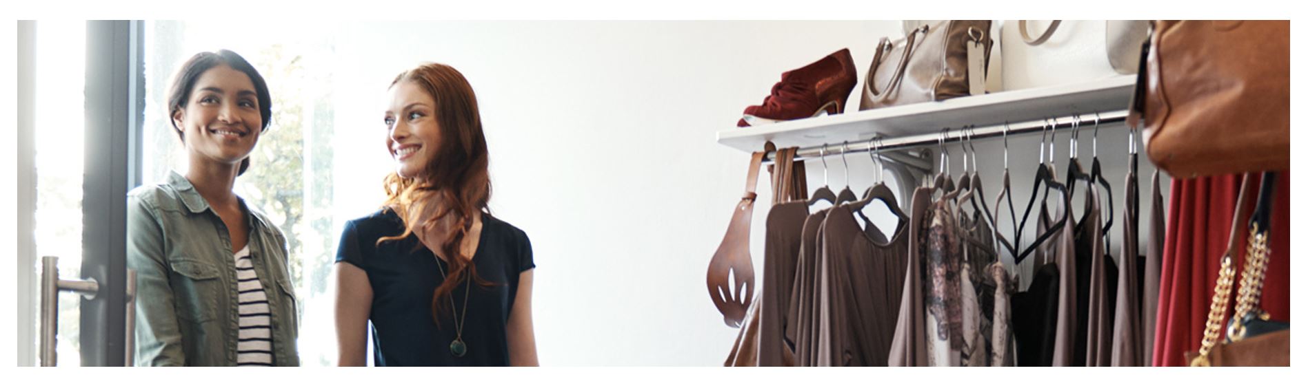 Two women shopping in boutique clothing store, browsing dresses and handbags on rack, retail fashion shopping experience