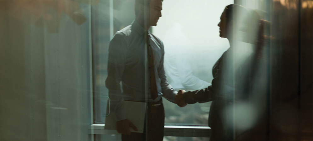 Business handshake between two professionals in glass office corridor, symbolizing partnership, deal closing, and corporate agreement in modern workplace