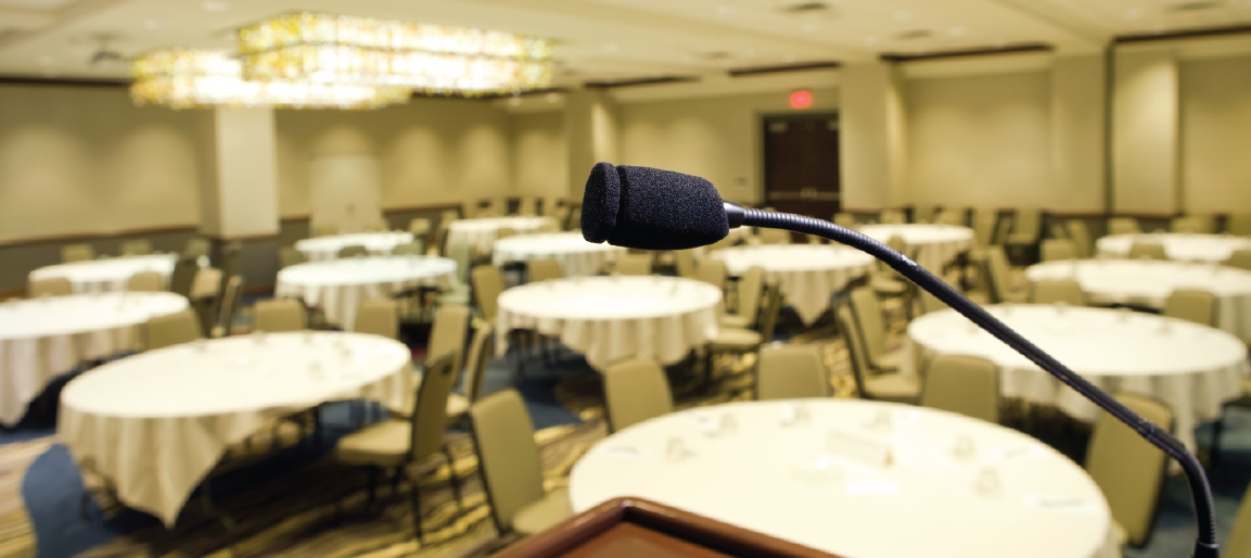 Podium microphone in empty hotel banquet conference room with round tables and chairs, event venue setup for speeches, meetings, and presentations.