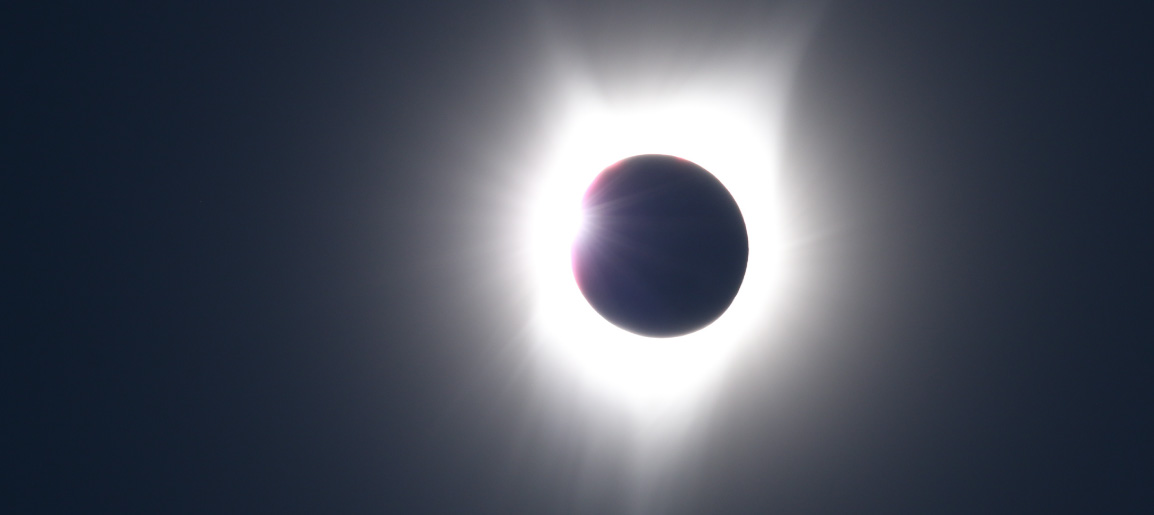 Solar eclipse with moon silhouetted against bright corona in dark sky, dramatic astronomy and celestial event photography