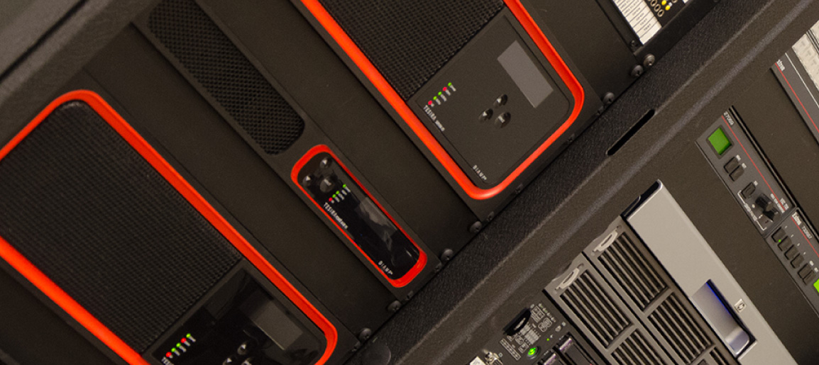 Rack-mounted AV equipment with status LEDs and control panels, showing professional audio processing and system hardware in equipment rack