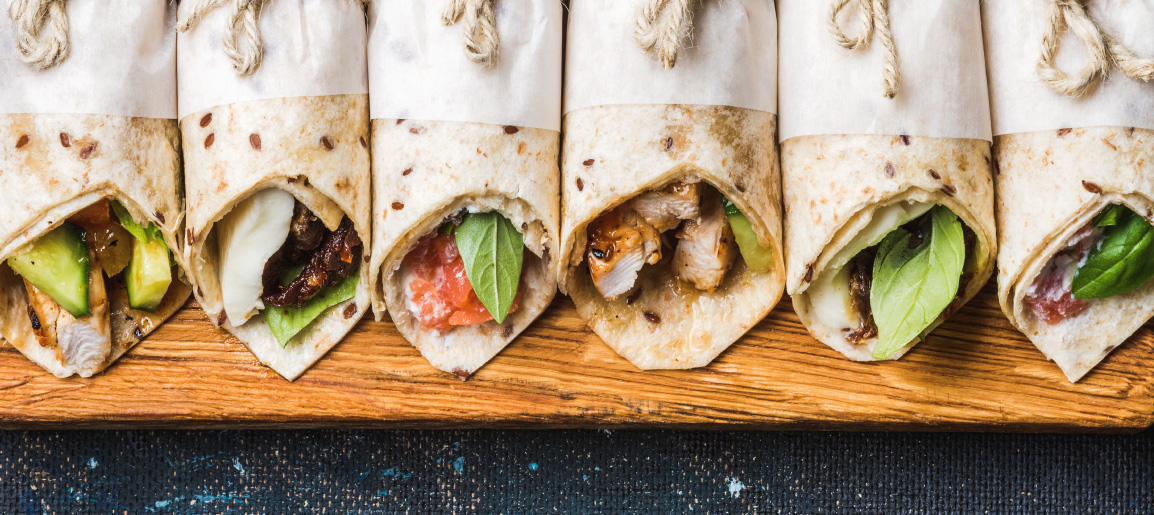 Assorted tortilla wraps on wooden board with fresh basil, chicken, vegetables and cheese, perfect for lunch, catering or party platter