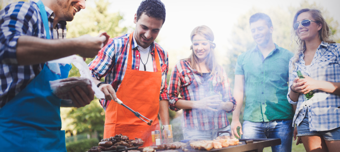 Friends grilling at outdoor barbecue in park, cooking food on BBQ and smiling together, summer weekend gathering and picnic scene