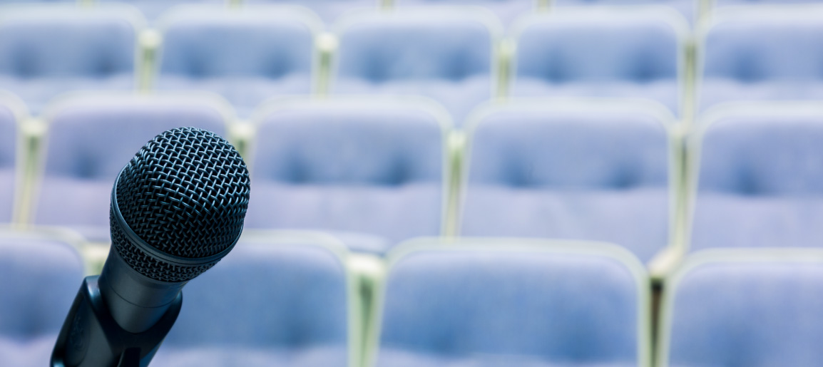Close-up of microphone on stage with empty auditorium seats in background, ideal for public speaking, conference, or event presentation