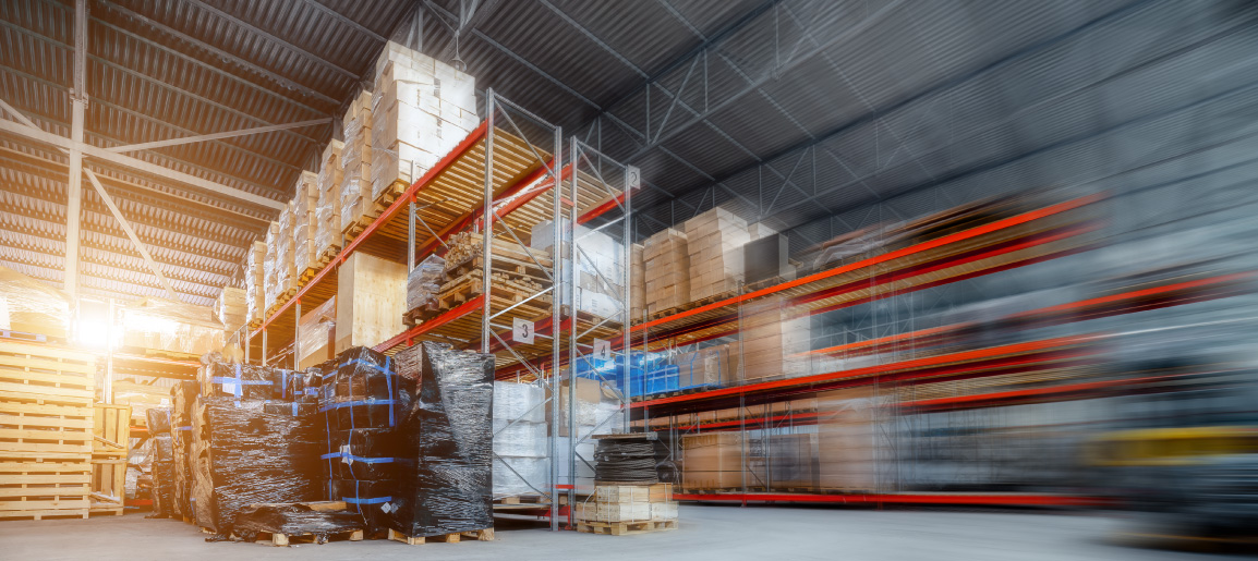 Busy warehouse interior with pallet racks and stacked boxes, showing logistics storage and blurred forklift motion in distribution center