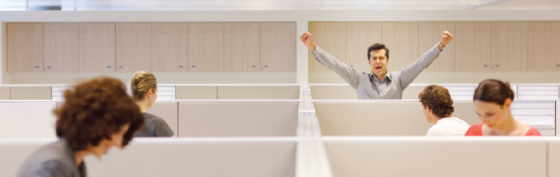 Man yawning and stretching in open-plan office cubicles while coworkers work, highlighting workplace fatigue and office productivity issues