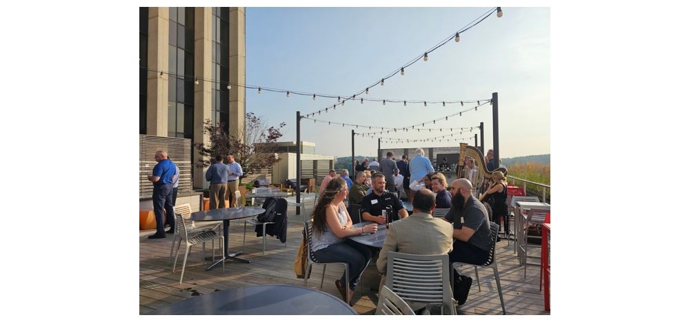 Outdoor rooftop networking event with people socializing at tables under string lights, corporate gathering and business mixer setting