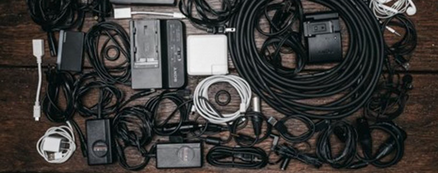 Messy collection of cables, chargers and adapters on desk, tangled wiring clutter for electronics, home office and IT cable management concept.