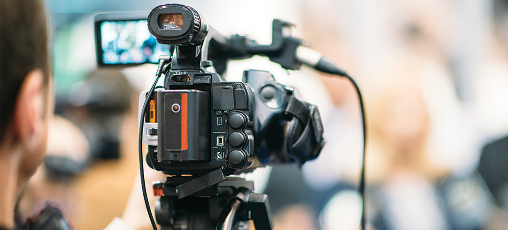 Professional video camera recording at conference or live event, capturing speaker on stage for broadcasting, streaming, and media production