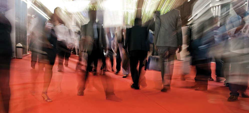 Blurred crowd walking on red carpet at trade show or conference, capturing busy event atmosphere, networking, and exhibition hall movement