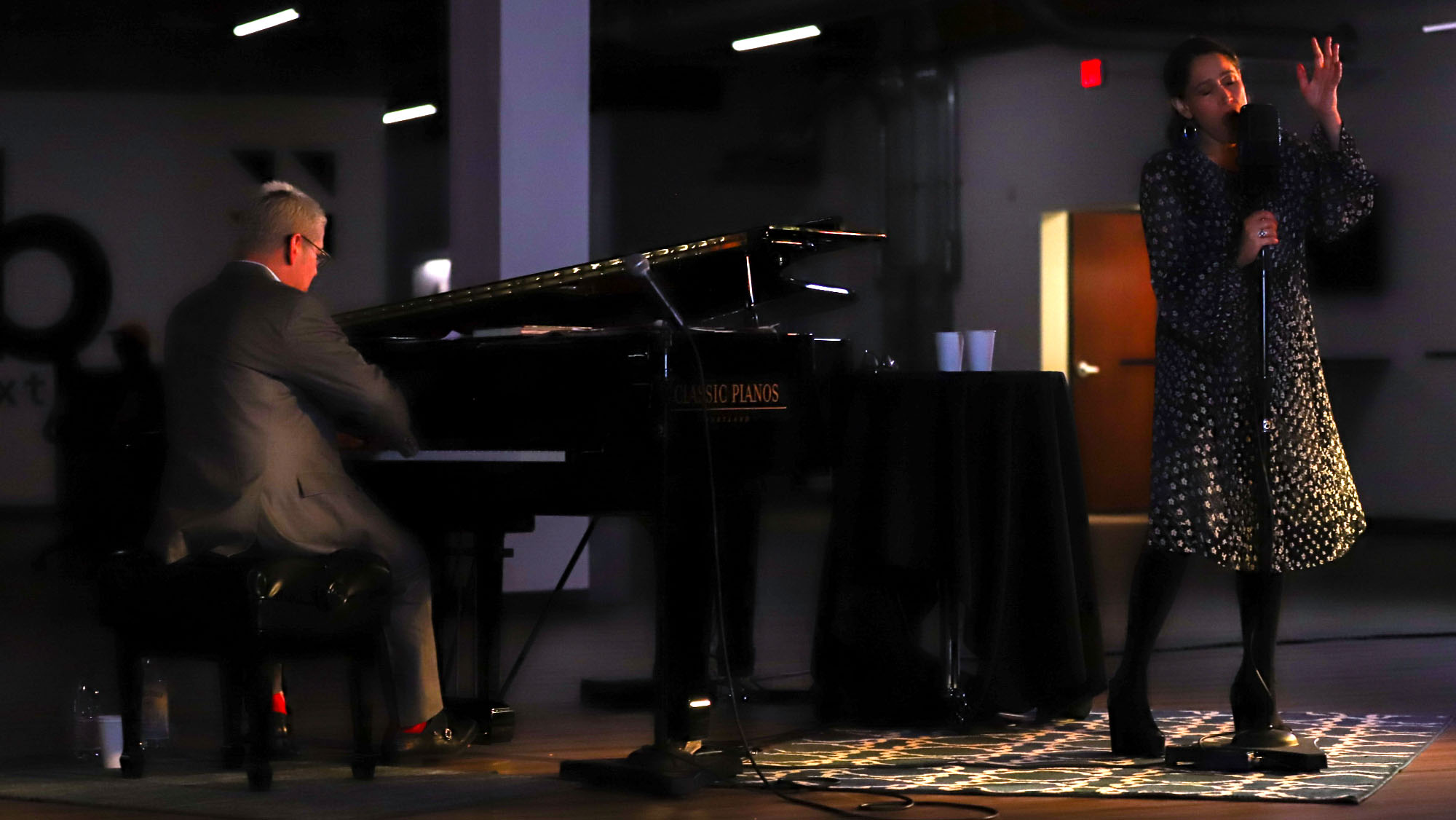 Pianist, Thomas Lauderdale, accompanying China Forbes on stage with grand piano and microphone, intimate live jazz performance in dimly lit venue.