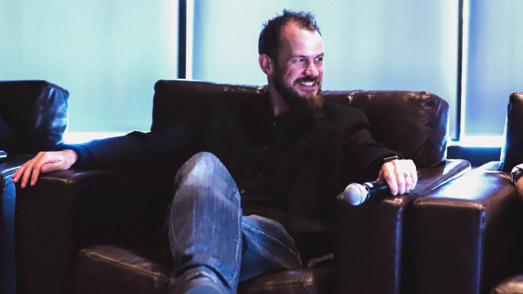 Image of a presenter seated with a mic in hand waiting to talk.