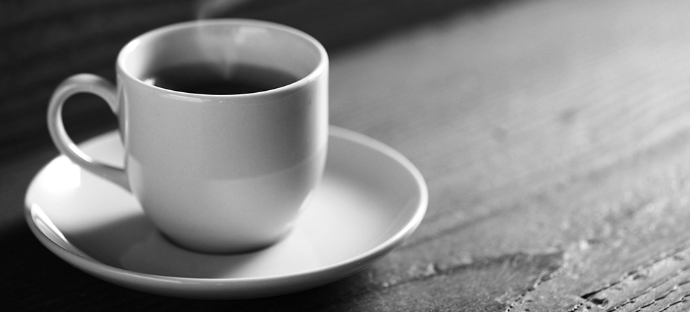 Black and white photo of hot coffee cup on saucer on rustic wooden table, cozy cafe mood and morning beverage close-up