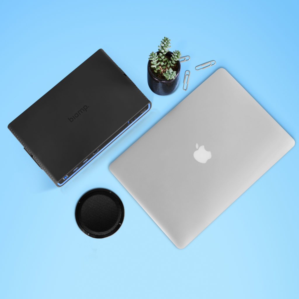 Top down image of a laptop, Biamp mic and Devio box, paper clips and a desk plant