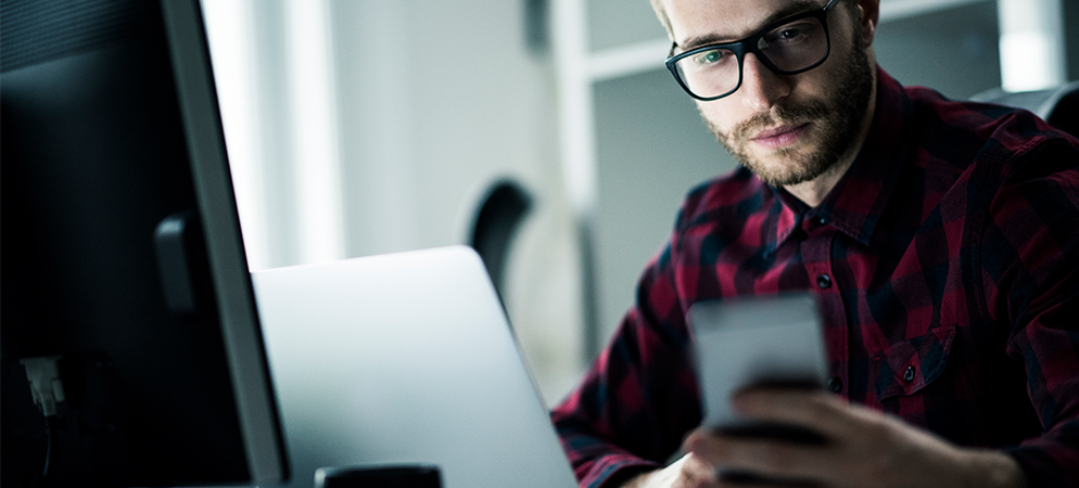 Man working at desk with laptop and smartphone in modern office, focused on digital tasks and productivity in a tech workspace