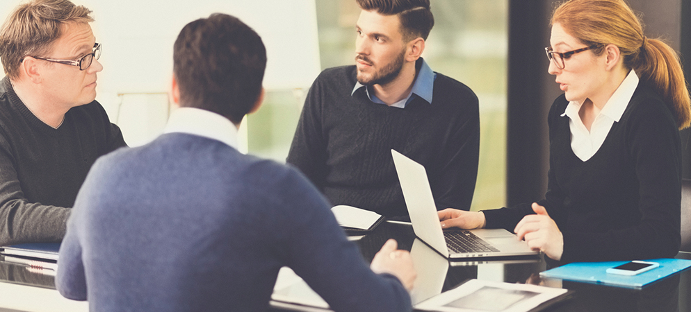 Business team meeting around table with laptop, discussing project strategy in modern office conference room