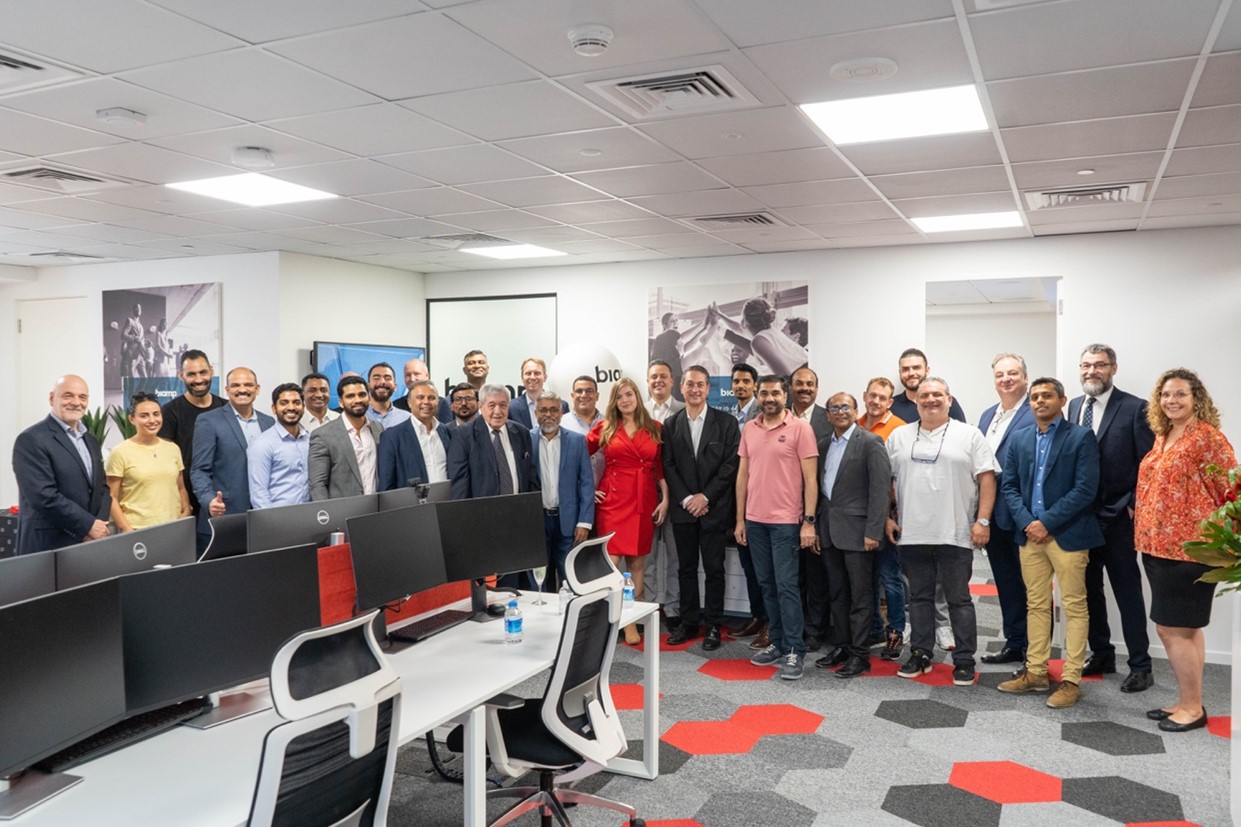 Biamp team group photo in modern office workspace with desks and monitors, employees and visitors gathered for corporate meeting and company event.