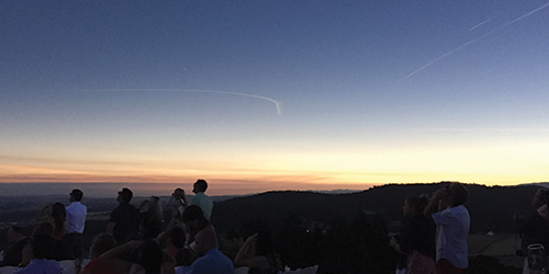 Image of a darkened sky due to a solar eclipse and people looking up at the sky.