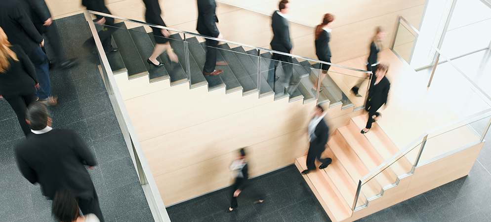 Blurred business people moving on office staircase, modern corporate building interior with glass railings, busy workplace commute and activity.