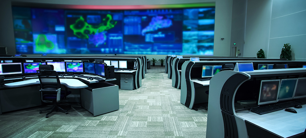 High-tech security operations center with multiple monitoring workstations and large video wall displaying real-time data and surveillance feeds