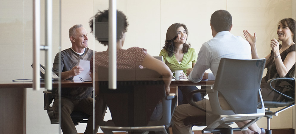 Business team meeting in glass conference room, coworkers discussing ideas around table in modern office collaboration space