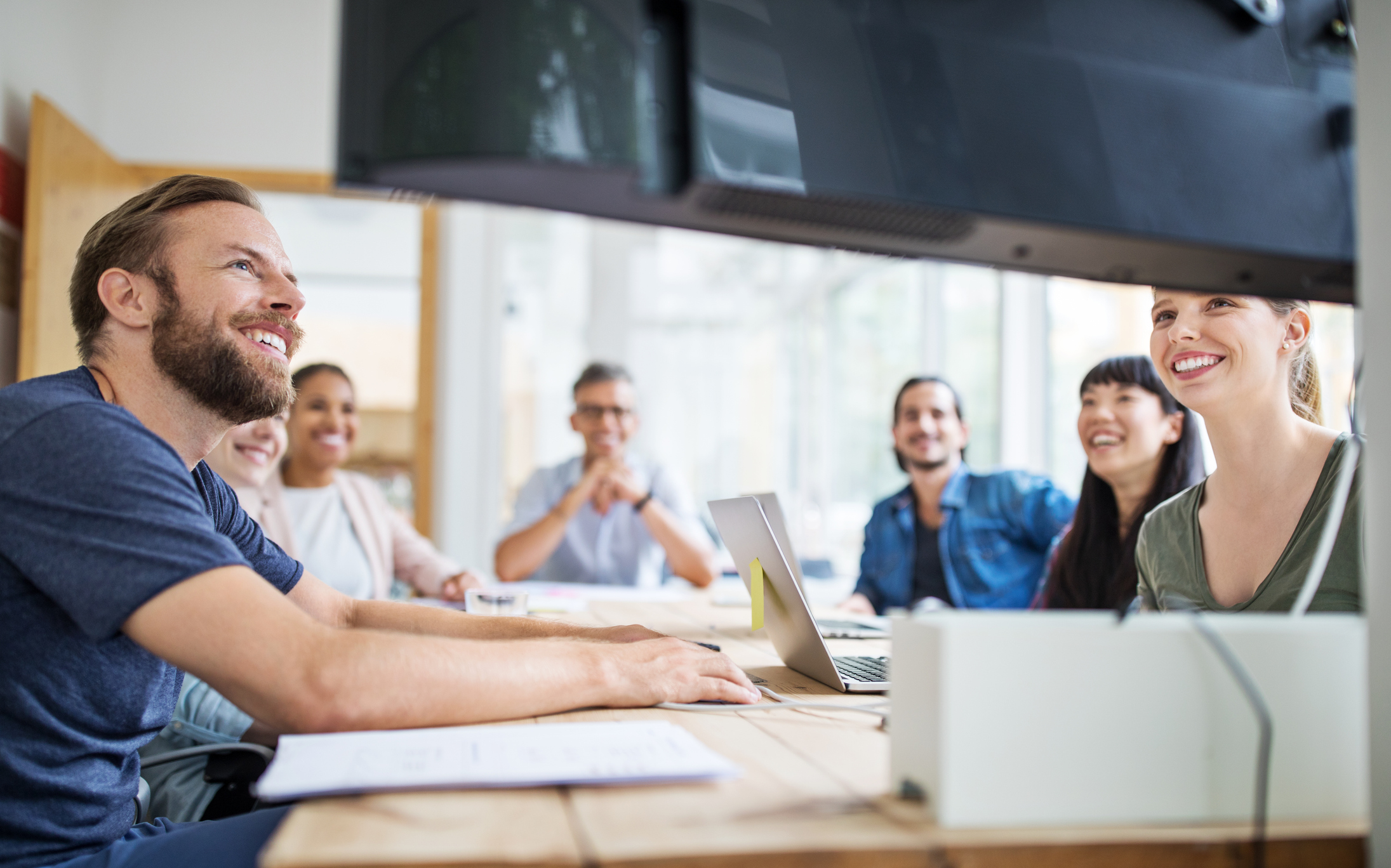 Team meeting in modern office conference room, coworkers collaborating and smiling during presentation on large screen