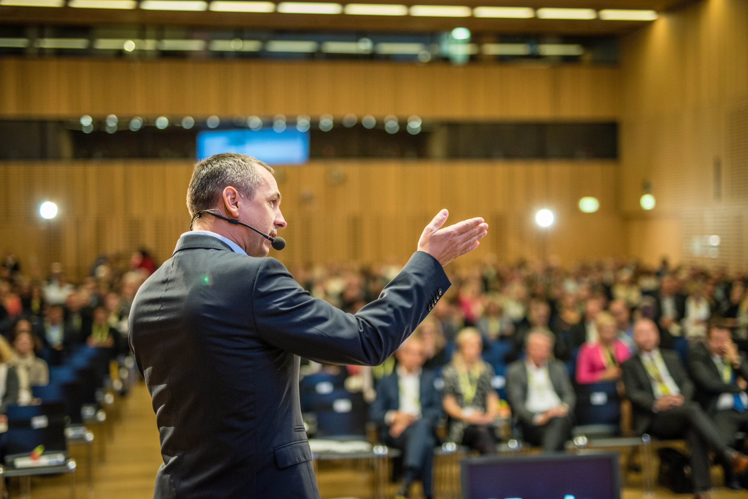 Keynote speaker with headset microphone presenting to large conference audience in auditorium during business event