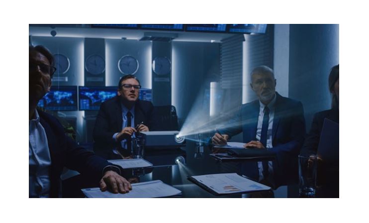 Business meeting in dark conference room with projector presentation, executives reviewing reports and data during corporate briefing