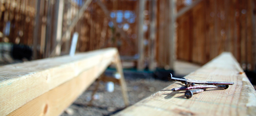 Close-up nails on wooden beam at construction site, home building framing in background, carpentry tools and residential development work.