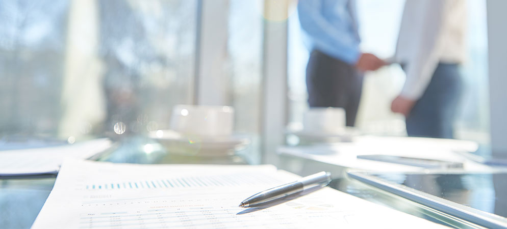 Pen on business documents on conference table with blurred colleagues in background, corporate meeting and office planning concept