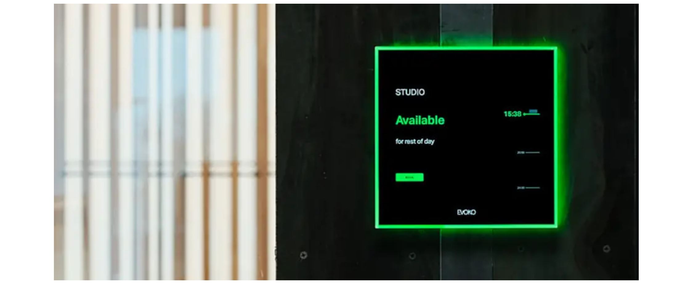 Evoko room booking display on office wall showing “Studio Available” with green status light for meeting room scheduling