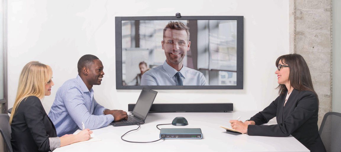 Team video conference meeting with remote participant on large display, laptops and tabletop speakerphone in modern boardroom setup