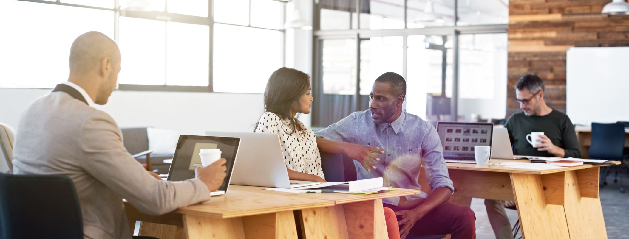 Coworkers collaborating in modern open office with laptops and coffee, team discussion and workplace productivity in shared workspace