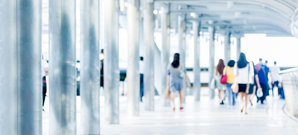 Blurred commuters walking through bright modern transit terminal with steel columns and glass architecture, conveying busy travel scene