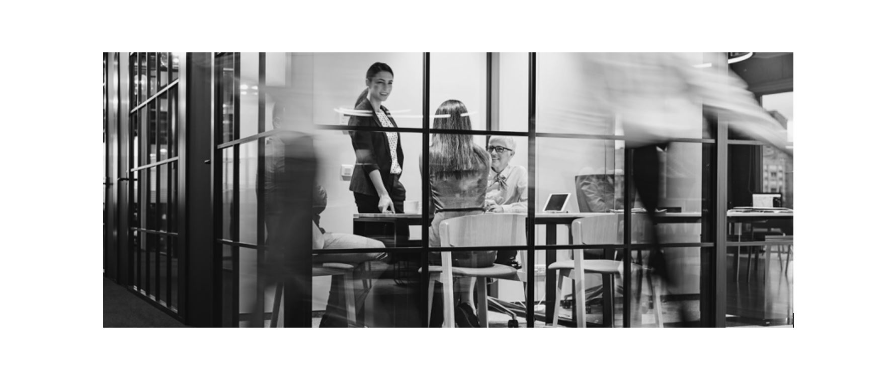 Team meeting in glass-walled conference room with blurred coworker walking by, modern office collaboration and workplace productivity
