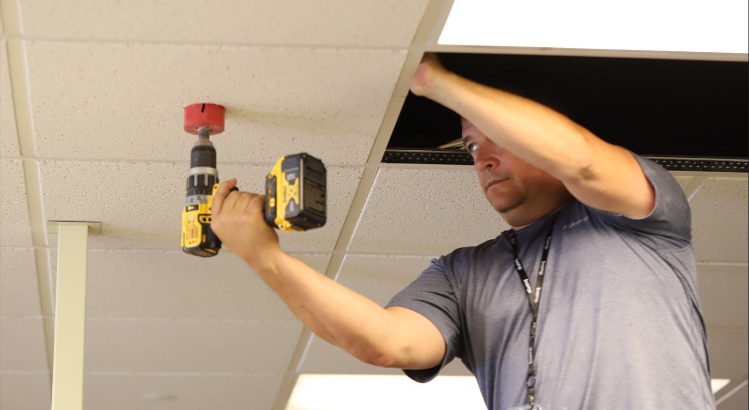 Technician installing ceiling-mounted AV hardware with power drill in office drop ceiling for conference room audio and video setup