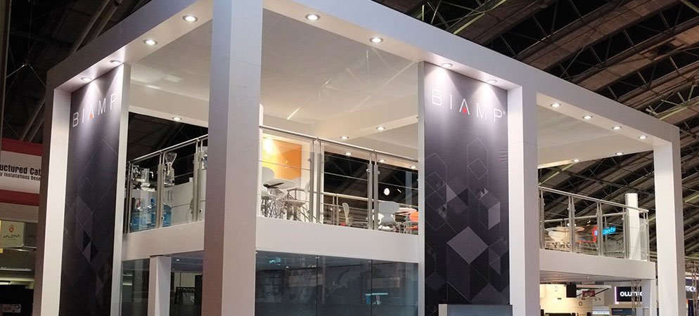 Biamp exhibition booth at trade show with two-story stand, branded banners, and modern lighting showcasing professional audio solutions