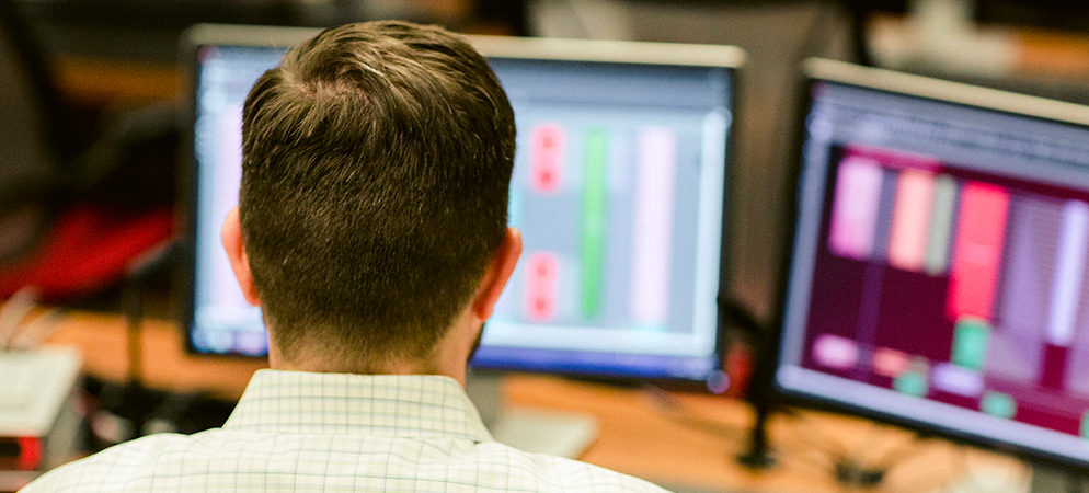Person monitoring dual computer screens with data dashboards, working in control room or IT operations center with real-time analytics display