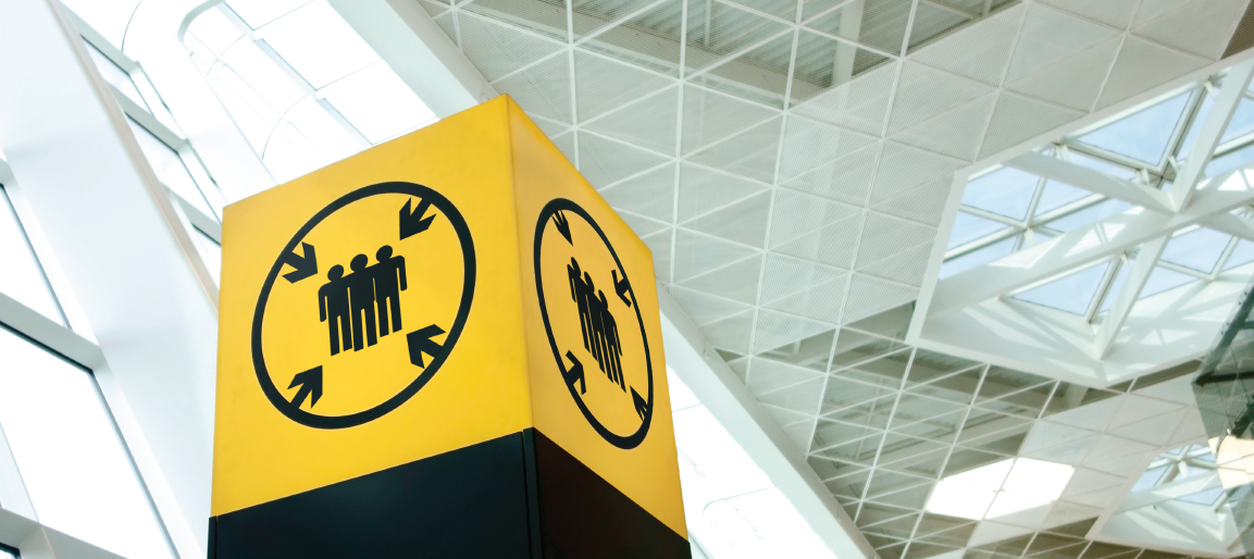 Airport terminal meeting point sign with people icon and arrows, inside modern glass-and-steel concourse with skylights