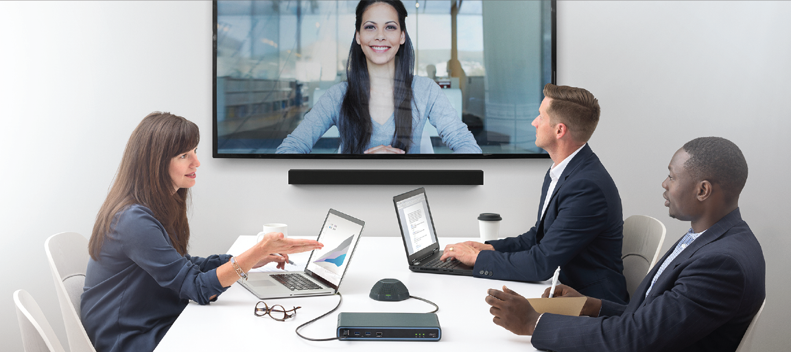 Business video conference in modern meeting room with remote presenter on screen, team collaboration using laptops and conferencing speakerphone.
