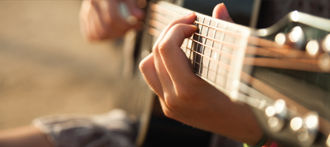 Close-up of hands playing acoustic guitar strings in warm sunlight, musician performing chords with shallow depth of field and bokeh