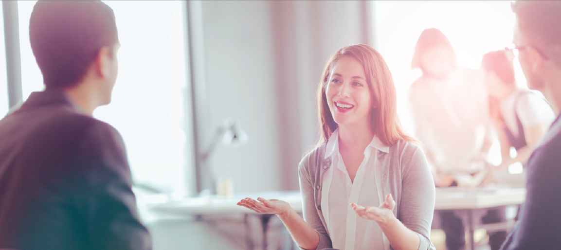 Smiling businesswoman talking with colleagues in bright office meeting, team discussion and workplace communication in modern workspace.