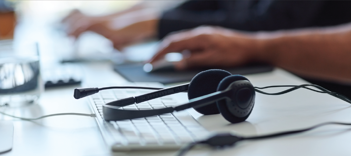 Call center headset on computer keyboard with agent working in background, customer support and business communication equipment setup.