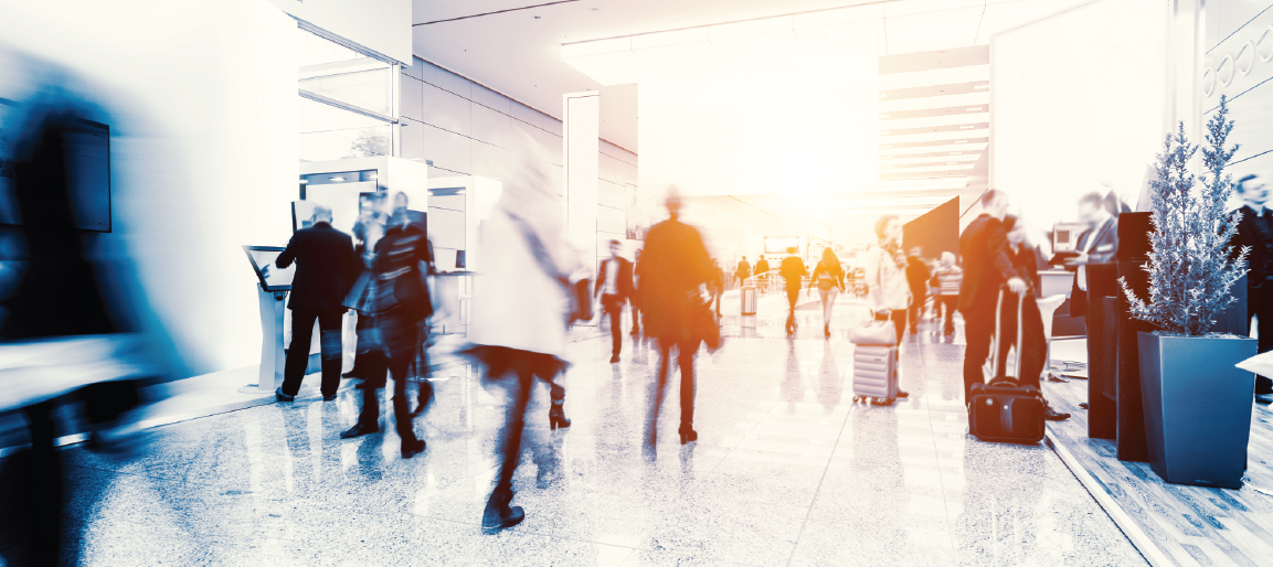 Busy convention center hallway with blurred attendees and luggage, modern trade show venue interior, networking crowd in bright expo space.