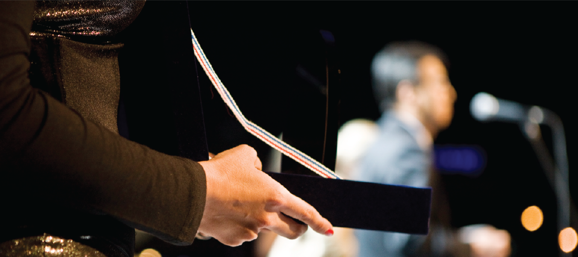 Close-up of hands holding award trophy on stage with speaker and microphone in background, corporate recognition ceremony and event presentation.